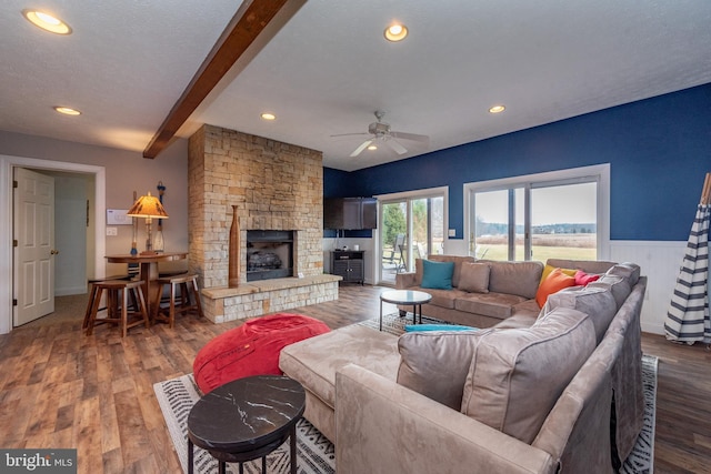 living room featuring ceiling fan, a fireplace, beamed ceiling, and dark wood-type flooring