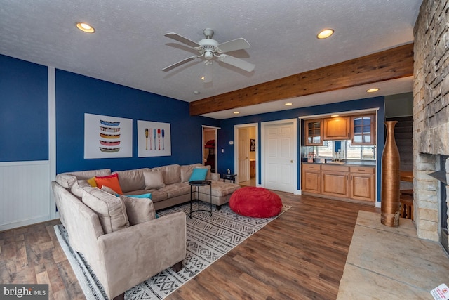 living room featuring ceiling fan, dark hardwood / wood-style flooring, beamed ceiling, a textured ceiling, and a fireplace