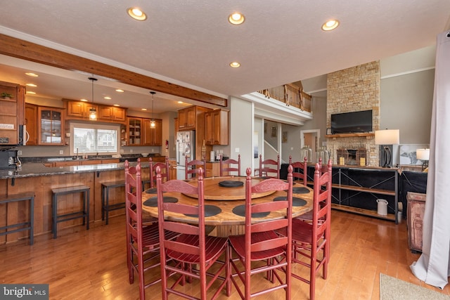 dining area featuring a textured ceiling, light hardwood / wood-style floors, a stone fireplace, and ornamental molding