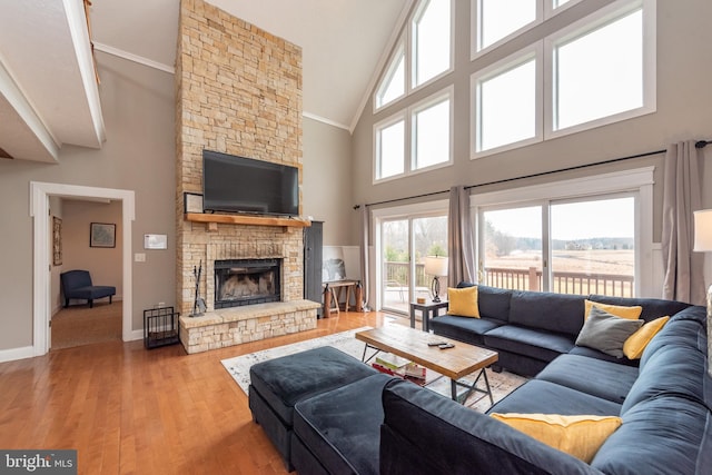 living room featuring crown molding, a fireplace, a high ceiling, and light hardwood / wood-style flooring