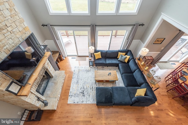 living room featuring hardwood / wood-style flooring, a wealth of natural light, a stone fireplace, and a high ceiling