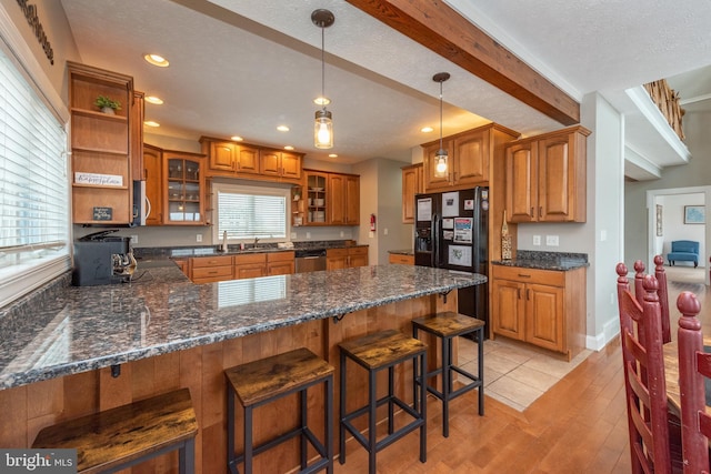 kitchen featuring black refrigerator with ice dispenser, stainless steel dishwasher, light wood-type flooring, a textured ceiling, and kitchen peninsula