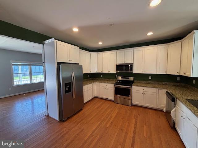 kitchen with hardwood / wood-style flooring, white cabinetry, appliances with stainless steel finishes, and dark stone counters