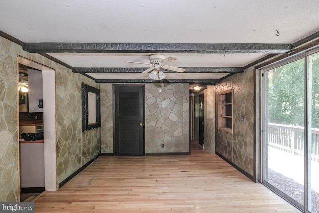 empty room featuring ceiling fan, light hardwood / wood-style flooring, and beamed ceiling