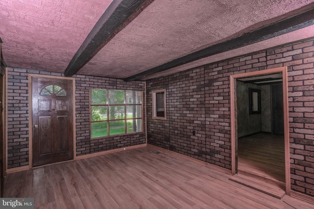 foyer entrance with beamed ceiling, wood-type flooring, and brick wall