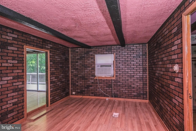 unfurnished room with beamed ceiling, brick wall, cooling unit, a textured ceiling, and hardwood / wood-style flooring