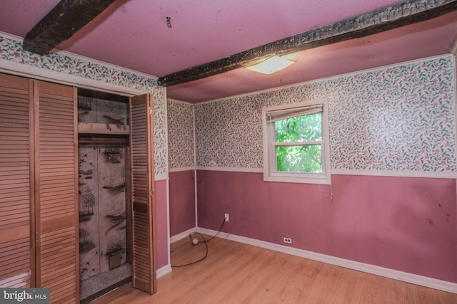 unfurnished bedroom featuring beam ceiling, a closet, wood-type flooring, and ornamental molding