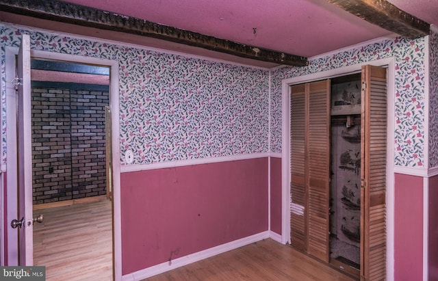 unfurnished bedroom with a closet, beamed ceiling, and hardwood / wood-style flooring