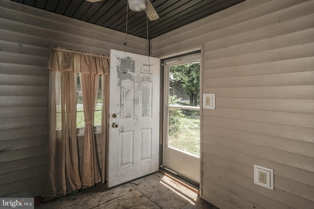 doorway with ceiling fan and wood walls