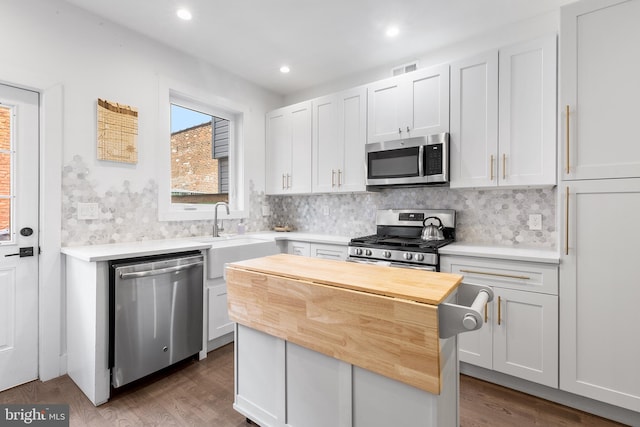 kitchen with stainless steel appliances, tasteful backsplash, hardwood / wood-style flooring, and wooden counters