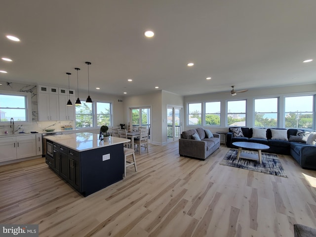 kitchen featuring ceiling fan, a kitchen island, light hardwood / wood-style flooring, pendant lighting, and white cabinets