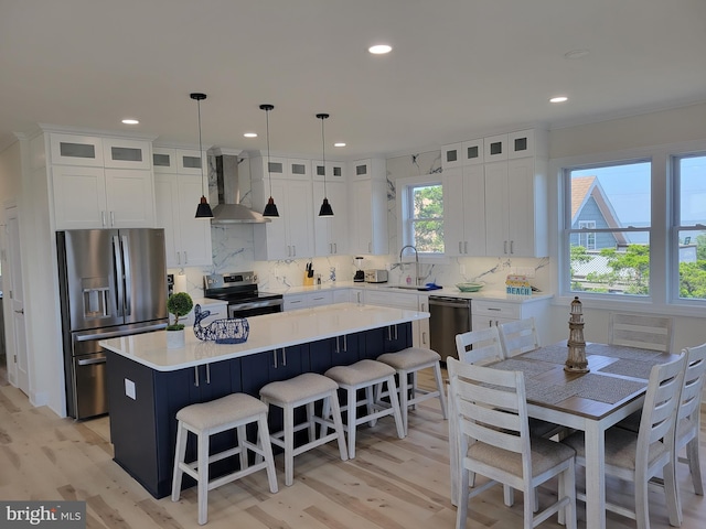 kitchen featuring a center island, hanging light fixtures, wall chimney exhaust hood, appliances with stainless steel finishes, and white cabinetry