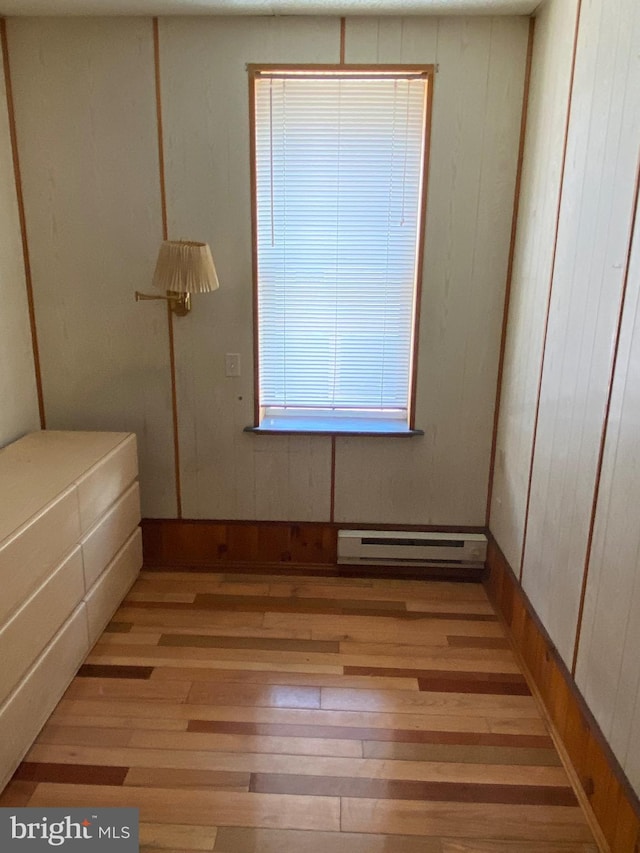 unfurnished bedroom featuring wood walls, light hardwood / wood-style flooring, and a baseboard heating unit