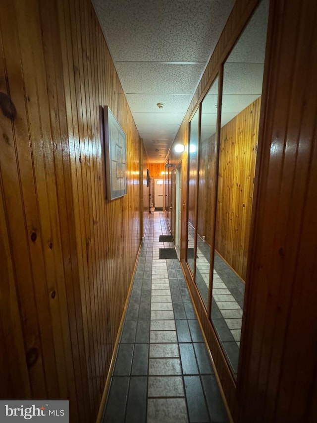 corridor featuring wooden walls and dark tile patterned floors