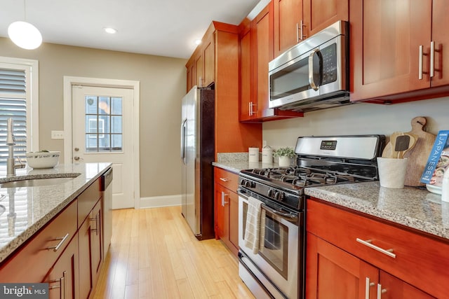 kitchen featuring sink, stainless steel appliances, light stone counters, light hardwood / wood-style floors, and decorative light fixtures