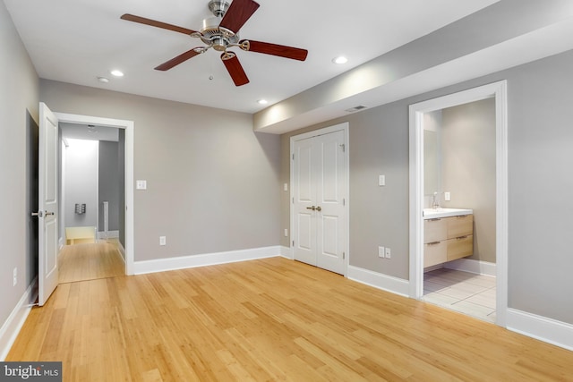 unfurnished bedroom featuring connected bathroom, ceiling fan, a closet, and light wood-type flooring