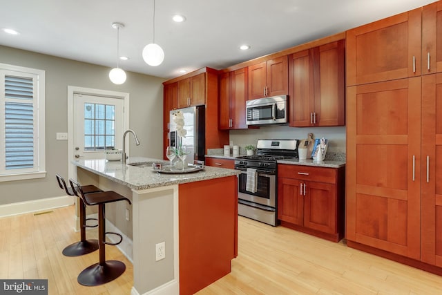 kitchen featuring light stone countertops, stainless steel appliances, pendant lighting, a kitchen bar, and a kitchen island with sink