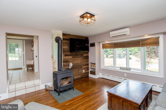 living room featuring wood walls, a wood stove, baseboard heating, a wall mounted AC, and hardwood / wood-style flooring