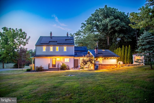 back house at dusk featuring solar panels and a yard