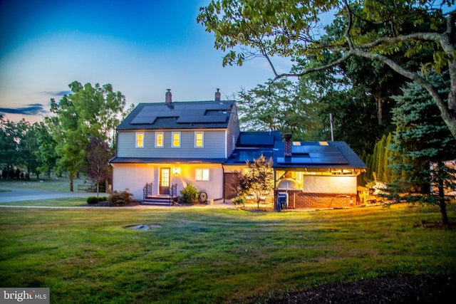 back house at dusk featuring a yard and solar panels