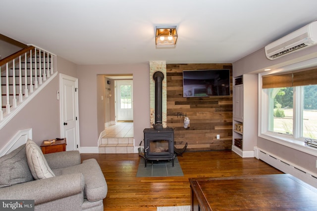 living room featuring a baseboard heating unit, hardwood / wood-style flooring, a wood stove, and a wall unit AC