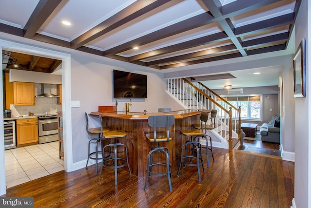 bar featuring backsplash, stainless steel stove, wall chimney exhaust hood, wine cooler, and beamed ceiling