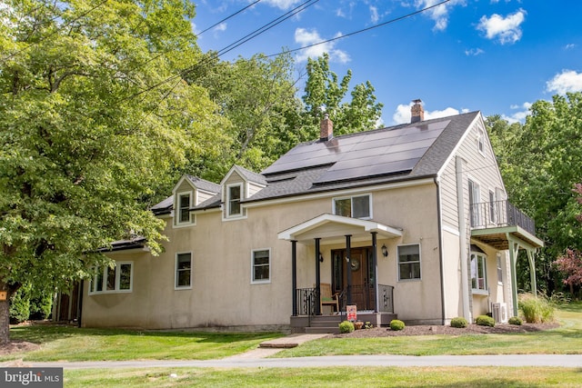 view of front of property with a balcony, a front yard, solar panels, and cooling unit