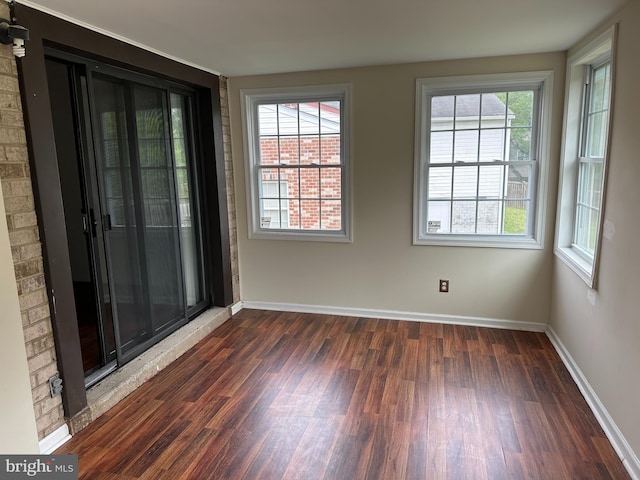 empty room with a wealth of natural light and dark hardwood / wood-style flooring