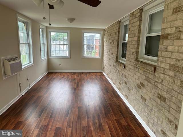 empty room featuring ceiling fan, dark wood-type flooring, a wall mounted air conditioner, brick wall, and a fireplace