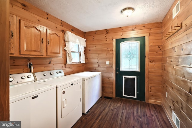 clothes washing area featuring wood walls, cabinets, a textured ceiling, and washing machine and clothes dryer