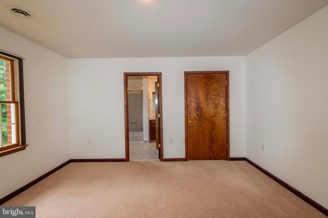 unfurnished bedroom featuring connected bathroom and light carpet