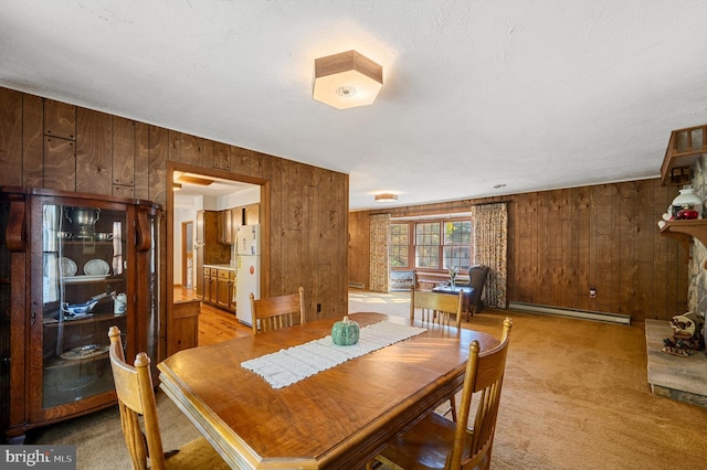 dining space with light carpet, a stone fireplace, wooden walls, and baseboard heating