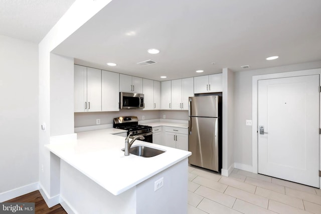 kitchen with sink, light tile patterned floors, kitchen peninsula, white cabinets, and appliances with stainless steel finishes