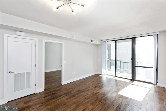 empty room with a notable chandelier, expansive windows, and dark wood-type flooring