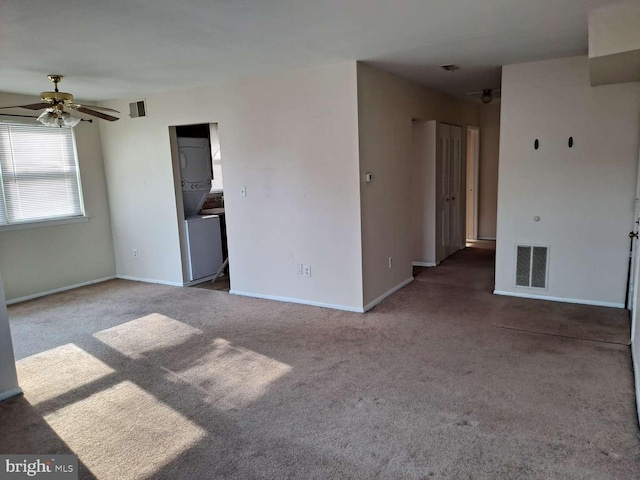 spare room featuring stacked washer and dryer, ceiling fan, and dark colored carpet