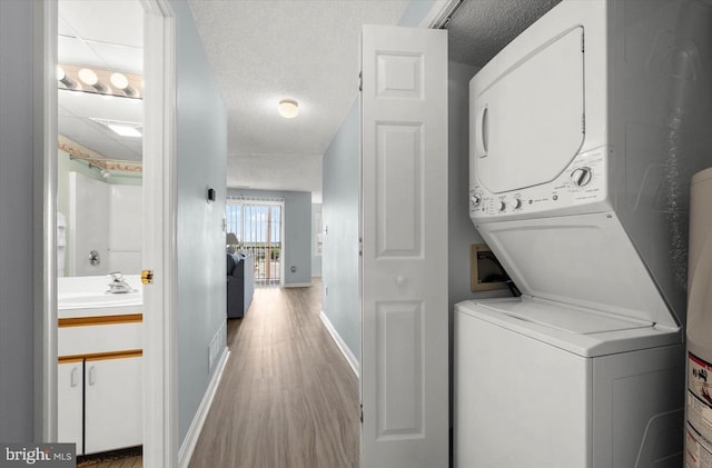 laundry room with a textured ceiling, sink, stacked washer / drying machine, and light wood-type flooring