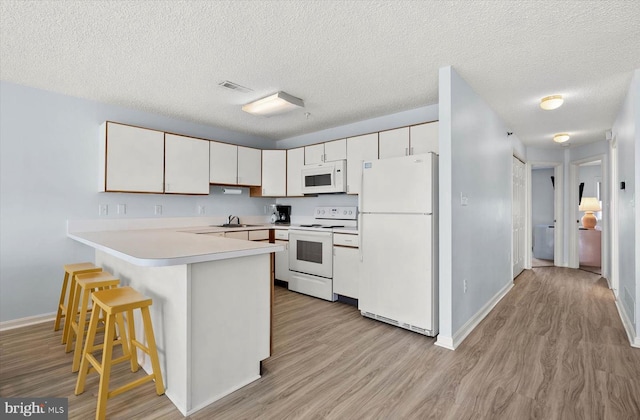 kitchen featuring light wood-type flooring, white appliances, a textured ceiling, white cabinets, and a breakfast bar area