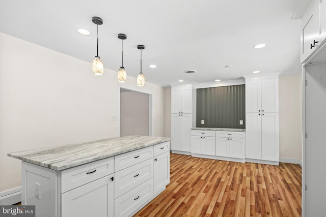 kitchen featuring light stone countertops, light hardwood / wood-style flooring, white cabinets, and decorative light fixtures