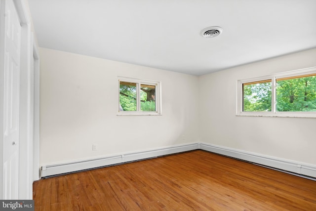 unfurnished room with hardwood / wood-style floors, baseboard heating, and a wealth of natural light