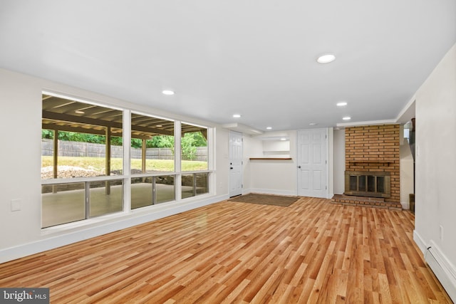 unfurnished living room with light hardwood / wood-style flooring, baseboard heating, and a brick fireplace