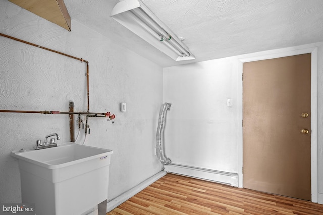 clothes washing area with a baseboard radiator, light hardwood / wood-style flooring, and sink