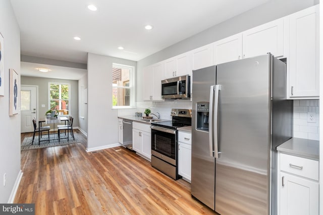 kitchen featuring white cabinets, light hardwood / wood-style floors, backsplash, and appliances with stainless steel finishes