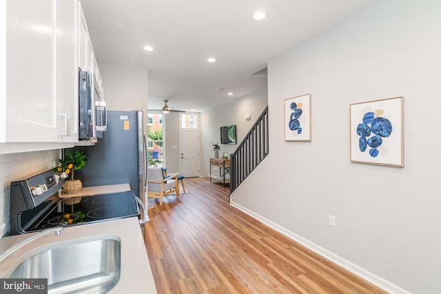 kitchen with hardwood / wood-style floors, stove, white cabinets, sink, and ceiling fan