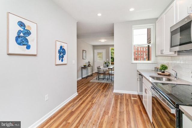 kitchen with decorative backsplash, appliances with stainless steel finishes, sink, light hardwood / wood-style flooring, and white cabinets