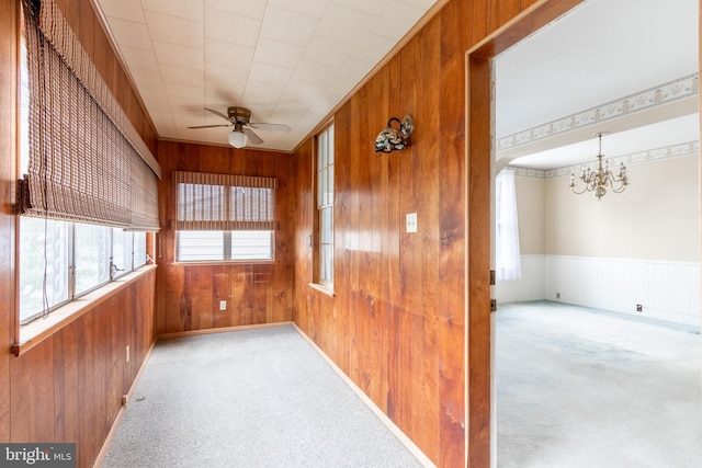 carpeted empty room with ceiling fan with notable chandelier and wooden walls