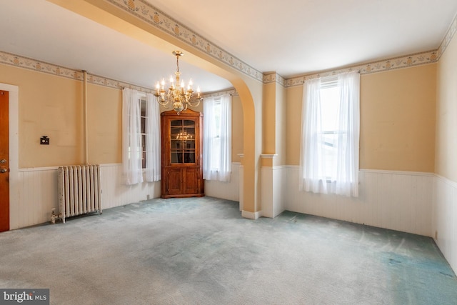 carpeted empty room featuring plenty of natural light, radiator, and a notable chandelier