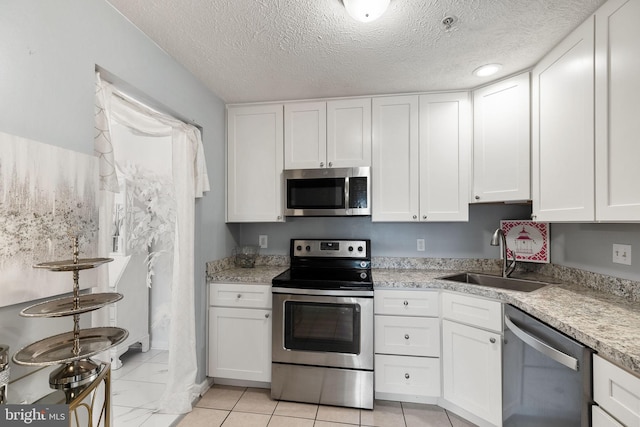 kitchen with white cabinets, sink, light tile patterned floors, a textured ceiling, and appliances with stainless steel finishes