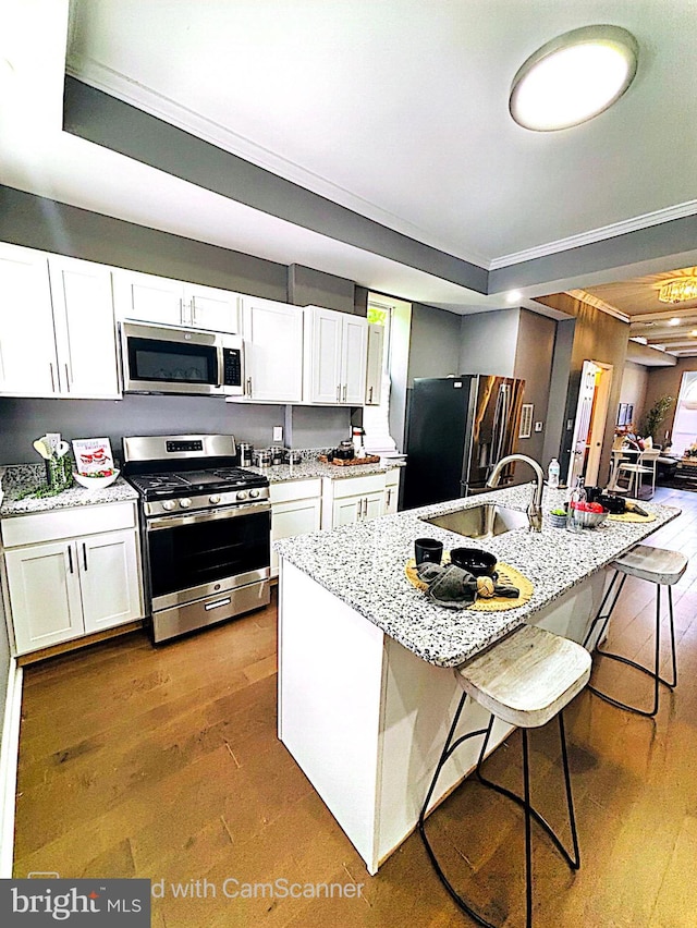 kitchen with appliances with stainless steel finishes, white cabinetry, hardwood / wood-style floors, and a breakfast bar area