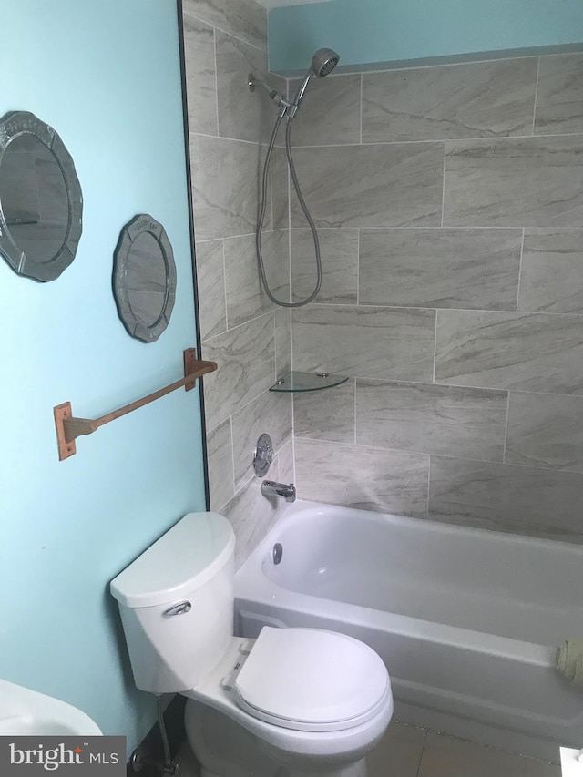 bathroom featuring tiled shower / bath, tile patterned flooring, and toilet