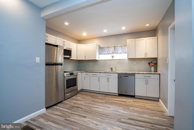 kitchen featuring tasteful backsplash, stainless steel appliances, light wood-type flooring, and a sink